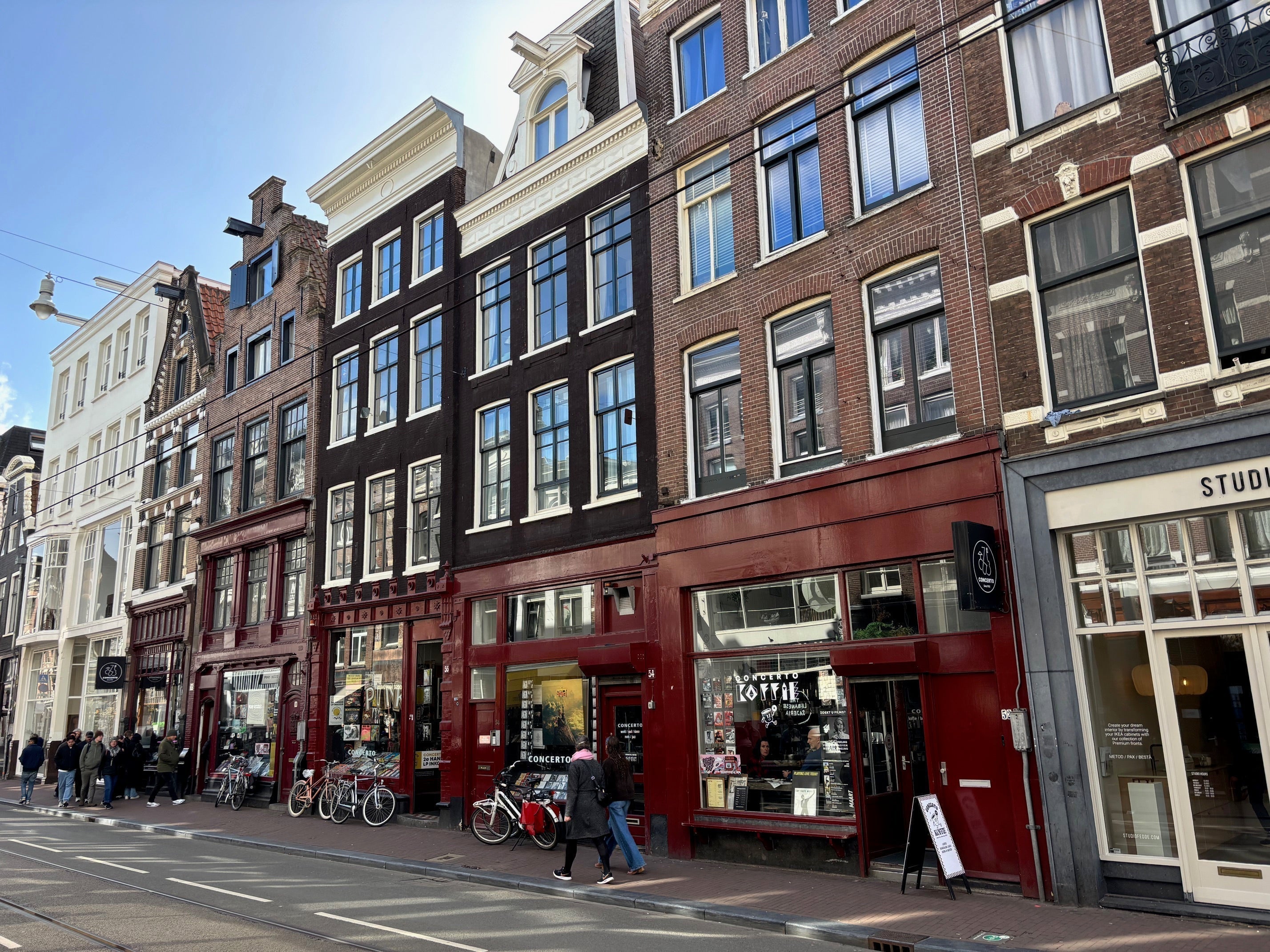 Rode gevel van platenzaak Concerto en Concerto Koffie aan de Utrechtsestraat in Amsterdam, met bezoekers en fietsen voor de winkel